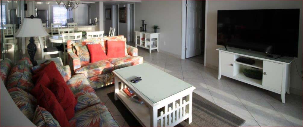 Living room area with colorful seating and large flatscreen TV, access to the private beachfront balcony.