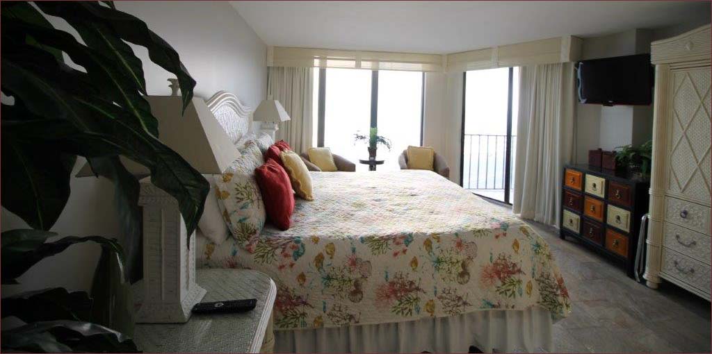 The generous master bedroom includes balcony access, 2 barrow chairs, flat screen tv and king bed.